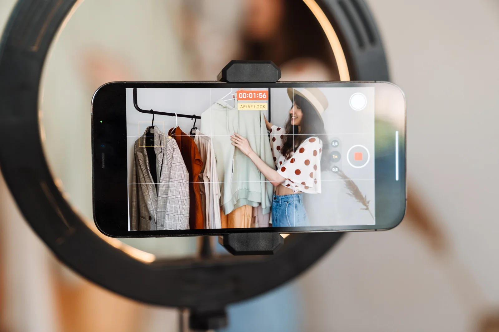 A creator records a clothing presentation on a phone inside a ring light